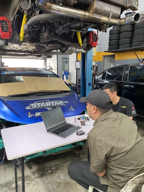 Juruteknik bengkel kereta sedang buat analisis data enjin dengan laptop di depan kereta atas lif